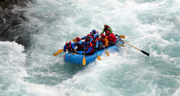 River rafting team navigating through turbulent waters, paddling through white foamy rapids against a scenic natural backdrop