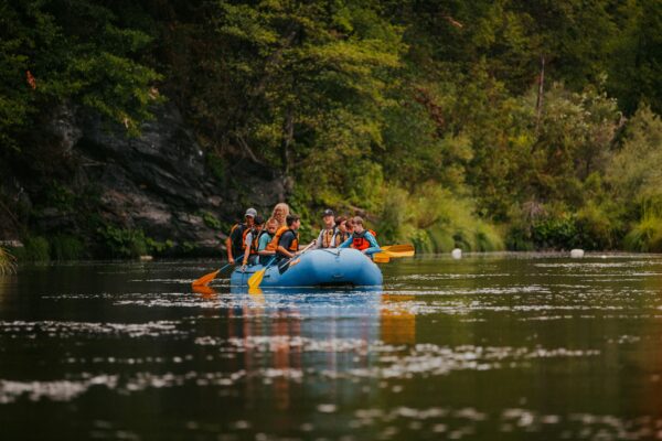 A group of rafters navigating turbulent rapids with determination and teamwork, surrounded by lush greenery and pristine river waters.